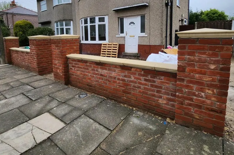 A red brick front garden wall with brick piers and pale coping stones outside a semi-detached house.