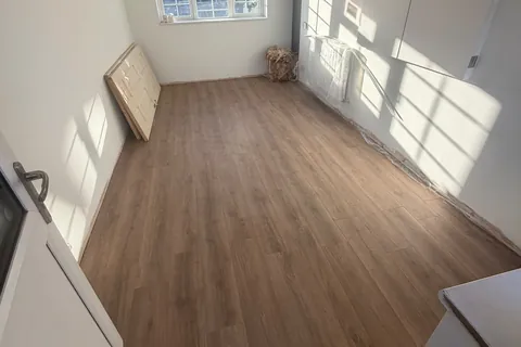 A converted garage room with white walls, timber beams and wood-effect flooring.