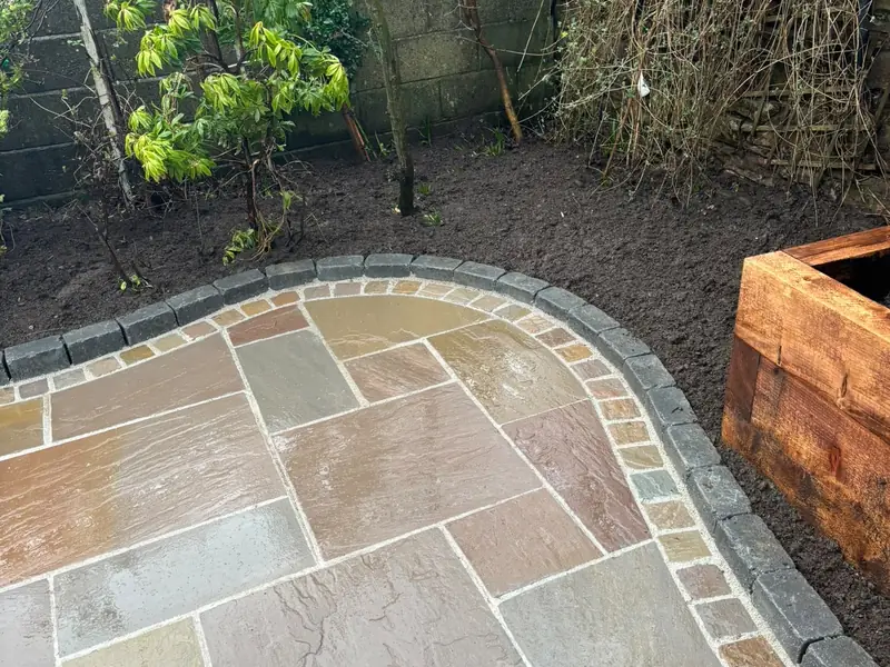 Curved patio edge of contrasting setts separating the paving from a planted border, with a timber sleeper raised bed.