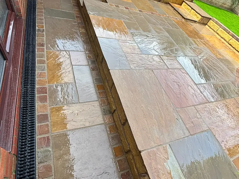 Natural stone paving on two levels, with a path, a raised paved area and a channel drain along the house.