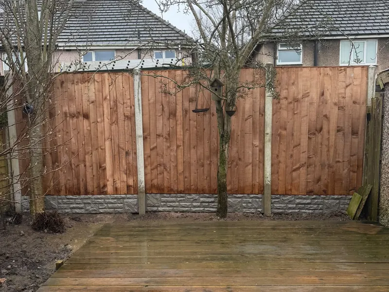 Vertical-board timber fence panels between concrete posts at the end of a garden with timber decking.