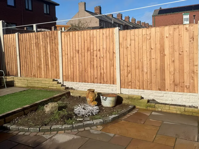 Vertical-board timber fence on concrete posts and gravel boards, behind a natural stone patio and planted bed.
