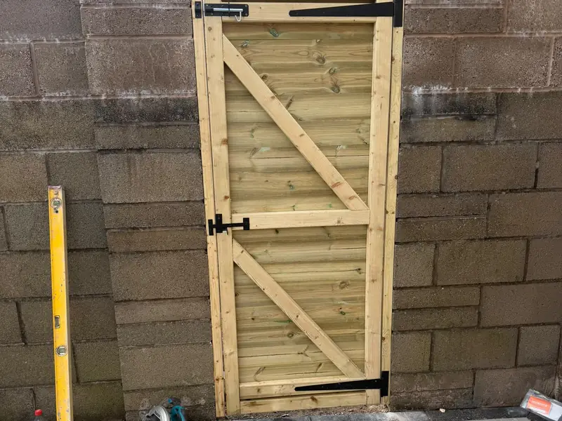 Timber gate in a block wall, with new porcelain paving laid in front of it.