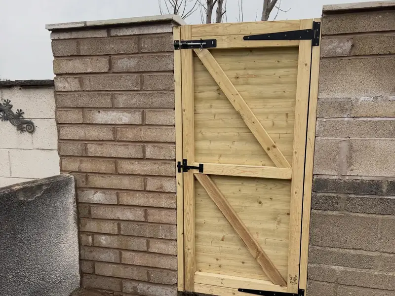 New timber garden gate hung between a brick pier and a block wall.