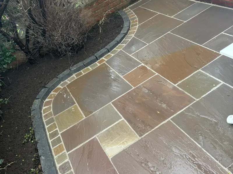 Natural stone patio with a curved edge of contrasting setts beside a planted border.