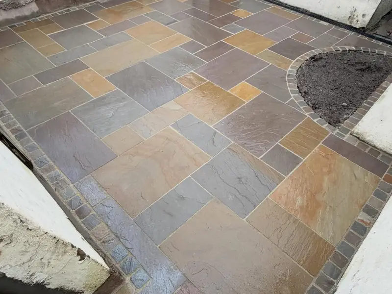 Indian stone patio in mixed buff, grey and rust tones, edged with a dark block border and a curved planting bed.