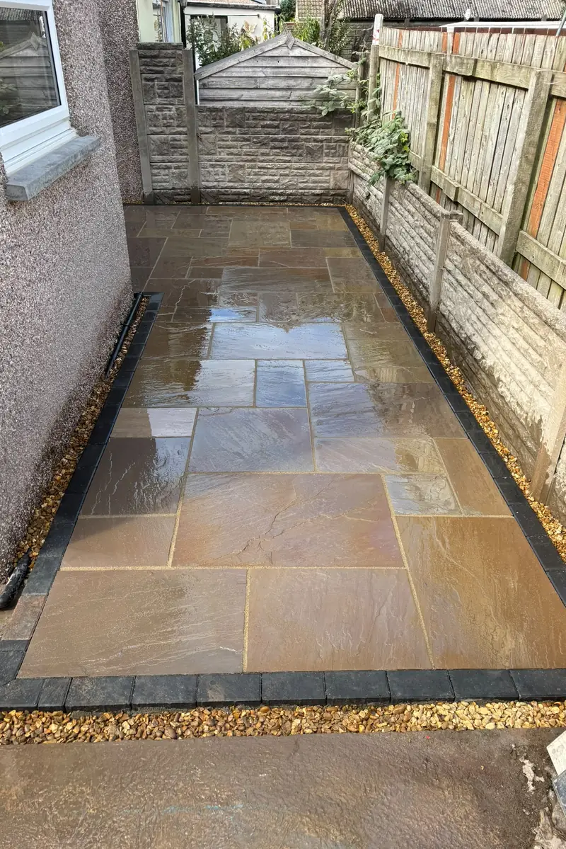 The same side garden with new natural stone paving, a dark block border and gravel edging.