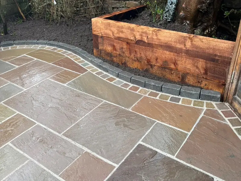 Paved patio with a curved edge of contrasting setts beside a timber sleeper raised bed.