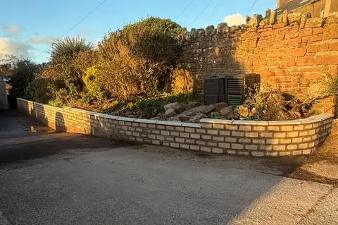 Block retaining wall topped with coping stones beside a raised garden bed.